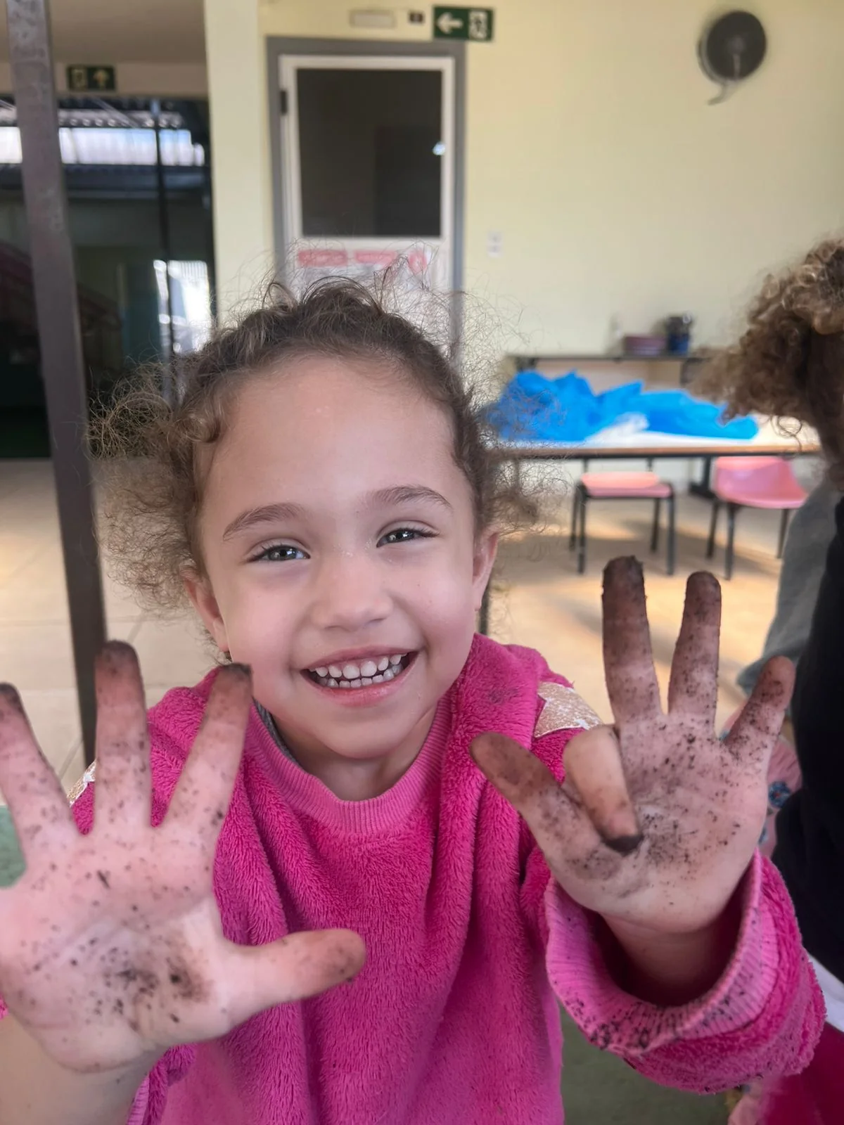 Criança sorrindo e mostrando as mãos depois de uma atividade de exploração na escola